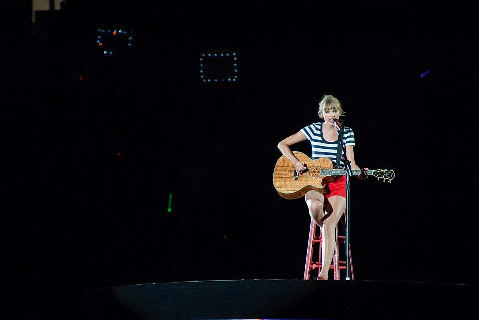 Taylor Swift wearing a striped shirt playing guitar on stage