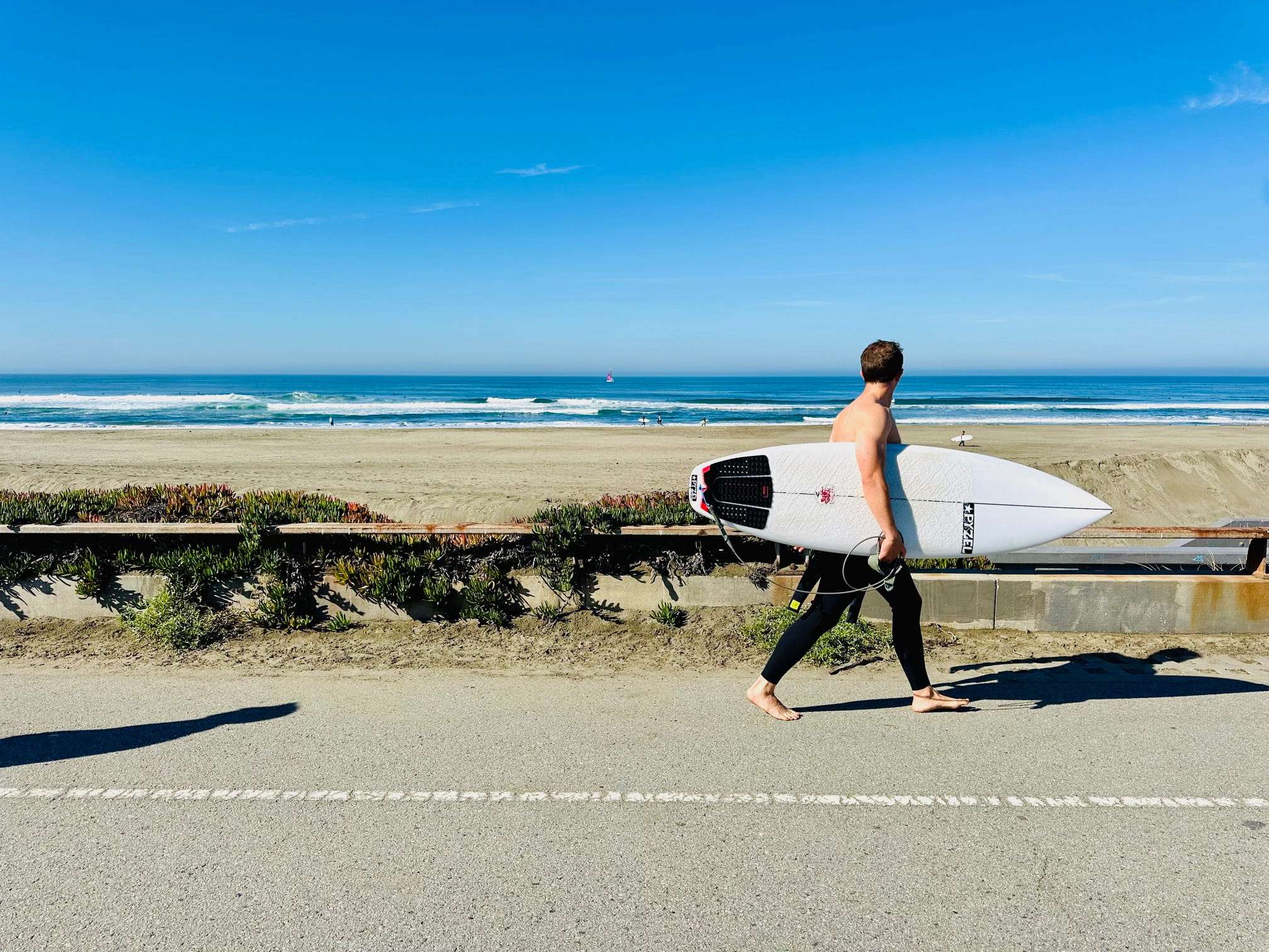 A surfer walks along the path at Sunset Dunes Park in San Francisco