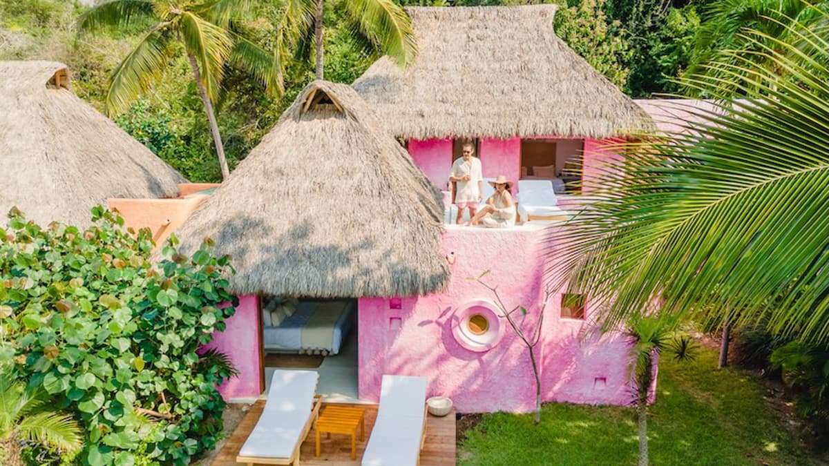 a pink villa with thatched roof and couple on the terrace