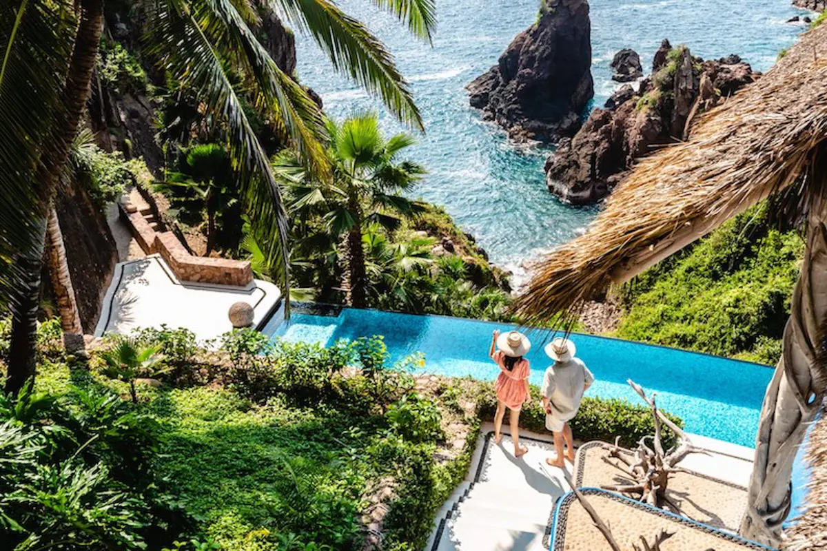 a hillside house with couple by a pool looking down at the ocean in mexico