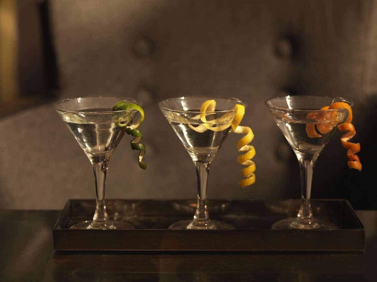 Three martini glasses with citrus twists on a serving tray