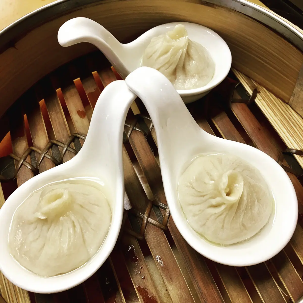 soup dumplings on white spoons in steaming basket