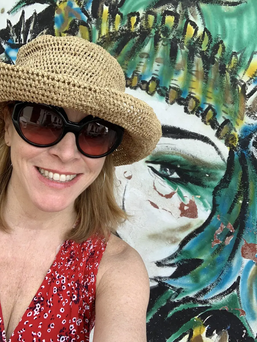 woman in hat and sunglasses in front of a colorful mural of a woman in panama city