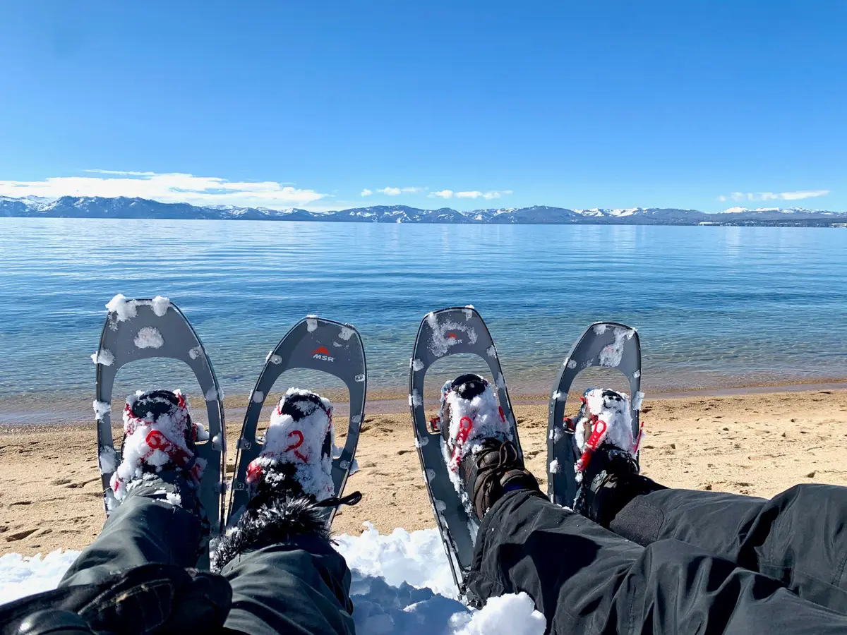 two sets of snowshoes on the beach with lake tahoe and mountains in the background