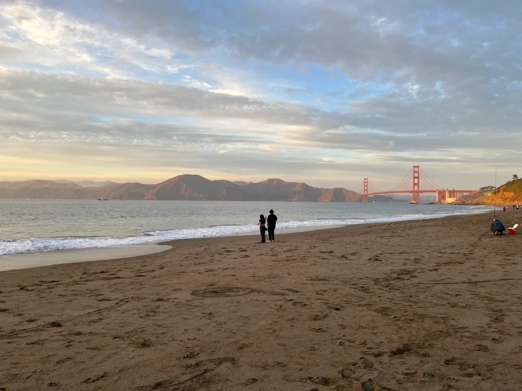 two people walking on baker beach in san francisco with golden gate bridge in the background