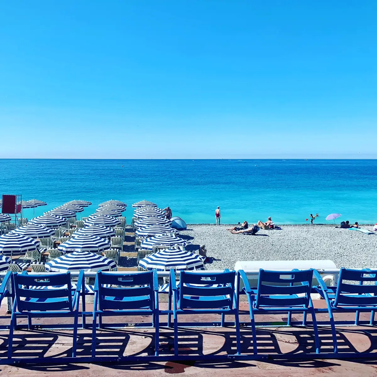 Nice, france, french riviera and its famous blue and white beach umbrellas in front of a turquoise sea