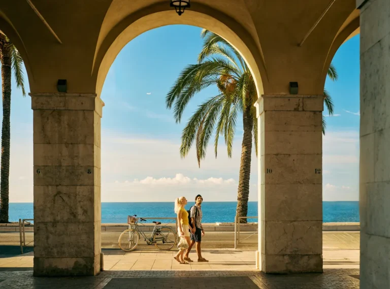 couple walking along the promenade des anglais in Nice, france, through the archways