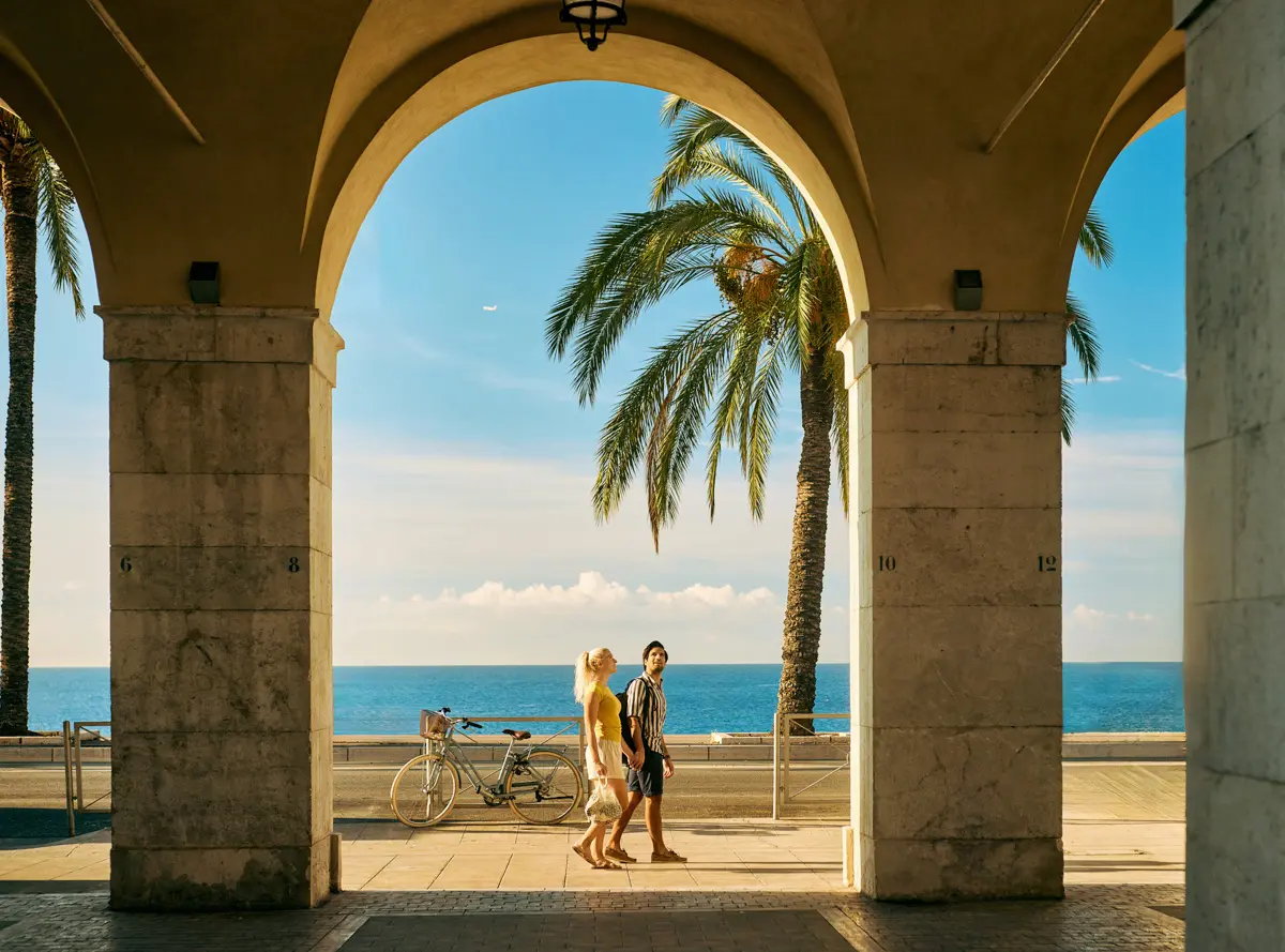 couple walking along the promenade des anglais in Nice, france, through the archways